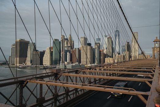 View of the Brooklyn Bridge with the Manhattan skyline steel suspension cables and traffic on the roadway under a cloudy sky in New York New York United States.