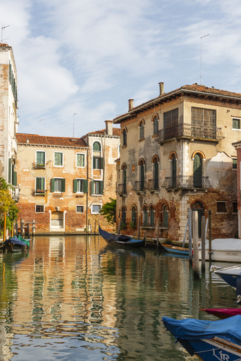 View of a quiet canal in Venice with historic weathered brick buildings traditional gondolas moored along the water and reflections on the canal surface Venice Veneto Italy. View of a quiet canal in Venice with historic weathered brick buildings traditional gondolas moored along the water and reflections on the canal surface Venice Veneto Italy.