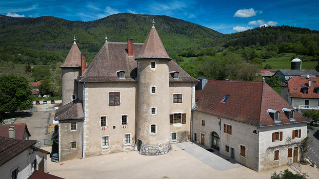 Aerial view of Chateau De Vesancy with its distinctive round towers and historic stone walls surrounded by lush green hills and a clear blue sky in Vesancy Auvergne Rhone Alpes France. Aerial view of Chateau De Vesancy with its distinctive round towers and historic stone walls surrounded by lush green hills and a clear blue sky in Vesancy Auvergne Rhone Alpes France.