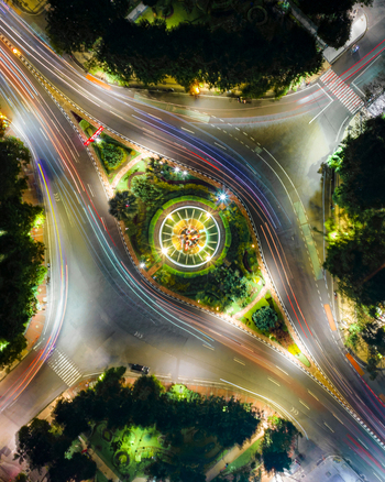 Aerial view of Monumen Bambu Runcing illuminated at night with vibrant light trails from traffic circling the roundabout in Kecamatan Genteng Jawa Timur Indonesia. Aerial view of Monumen Bambu Runcing illuminated at night with vibrant light trails from traffic circling the roundabout in Kecamatan Genteng Jawa Timur Indonesia.