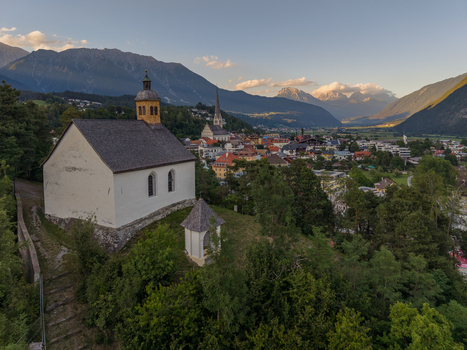 Aerial view of St. Laurentius Church situated on a hill overlooking the town of Imst with the surrounding Austrian Alps at golden hour in Imst Tyrol Austria.