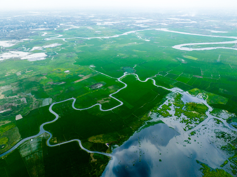 Aerial view of the winding river flowing through lush green agricultural fields and wetlands in Dhaka Dhaka Division Bangladesh. Aerial view of the winding river flowing through lush green agricultural fields and wetlands in Dhaka Dhaka Division Bangladesh.