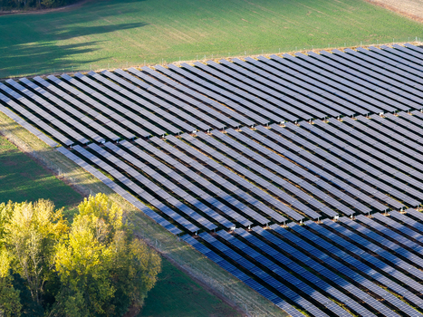 Aerial view of a large solar farm with rows of photovoltaic panels installed in a rural field surrounded by green agricultural land and trees in Woodburn Oregon United States. Aerial view of a large solar farm with rows of photovoltaic panels installed in a rural field surrounded by green agricultural land and trees in Woodburn Oregon United States.