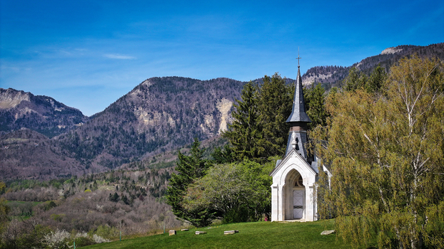 Aerial view of Chapelle Notre Dame de Riantmont a small white chapel with a pointed spire surrounded by lush green trees and rolling mountains in Vesancy Auvergne Rhone Alpes France. Aerial view of Chapelle Notre Dame de Riantmont a small white chapel with a pointed spire surrounded by lush green trees and rolling mountains in Vesancy Auvergne Rhone Alpes France.