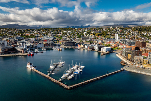 Aerial view of the harbor with sailboats moored at the pier modern and historic buildings along the waterfront and mountains in the background in Tromso Troms Norway.