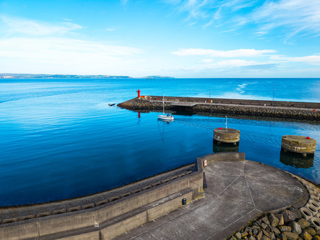 Aerial view of Bangor Harbour and Town with a small sailboat navigating the calm blue waters stone breakwaters and clear sky in Bangor Northern Ireland United Kingdom.
