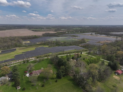 Lebanon United States 12 April 2026 Aerial view of a large solar farm array surrounded by green fields residential houses and dense trees under a cloudy sky.