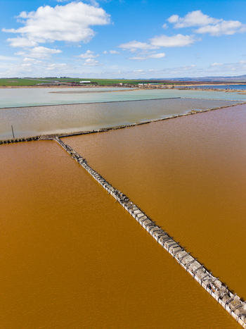 Aerial view of the pink salt pans of Lake Atanasovsko with stone paths dividing the colorful water under a blue sky in Burgas Burgas Bulgaria. Aerial view of the pink salt pans of Lake Atanasovsko with stone paths dividing the colorful water under a blue sky in Burgas Burgas Bulgaria.