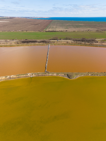 Aerial view of Lake Atanasovsko salt pans with bright yellow and orange evaporation ponds separated by a narrow dike with green fields and the Black Sea in Burgas Burgas Bulgaria. Aerial view of Lake Atanasovsko salt pans with bright yellow and orange evaporation ponds separated by a narrow dike with green fields and the Black Sea in Burgas Burgas Bulgaria.