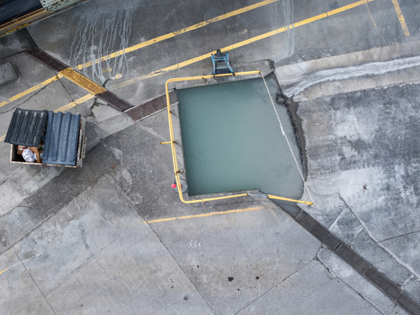 Aerial view of an industrial site featuring a rectangular water basin enclosed by yellow safety railings surrounded by concrete surfaces and a nearby dumpster in Melbourne VIC Australia.