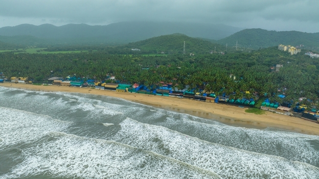 Aerial view of Palolem Beach with its sandy coastline lush palm trees and small beach huts under a cloudy sky in Canacona Goa India.