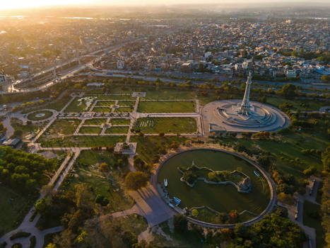Aerial view of Minar e Pakistan surrounded by lush parkland a circular pond and the sprawling city skyline under golden hour light in Lahore Punjab Pakistan.
