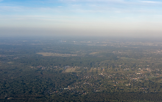 Aerial view of the expansive green forests and scattered urban development blending into the horizon creating a textured landscape under a hazy sky Warsaw Masovian Voivodeship Poland. Aerial view of the expansive green forests and scattered urban development blending into the horizon creating a textured landscape under a hazy sky Warsaw Masovian Voivodeship Poland.