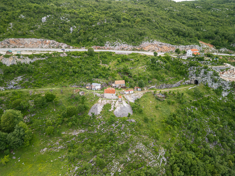 Aerial view of a small cluster of houses nestled on a rocky hillside with a road and a tunnel entrance in the background in Niksic Municipality Montenegro. Aerial view of a small cluster of houses nestled on a rocky hillside with a road and a tunnel entrance in the background in Niksic Municipality Montenegro.