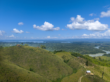 Aerial view of Shita Pahar featuring lush green hills small rustic huts and a winding river under a clear blue sky in Kaptai Chittagong Division Bangladesh. Aerial view of Shita Pahar featuring lush green hills small rustic huts and a winding river under a clear blue sky in Kaptai Chittagong Division Bangladesh.