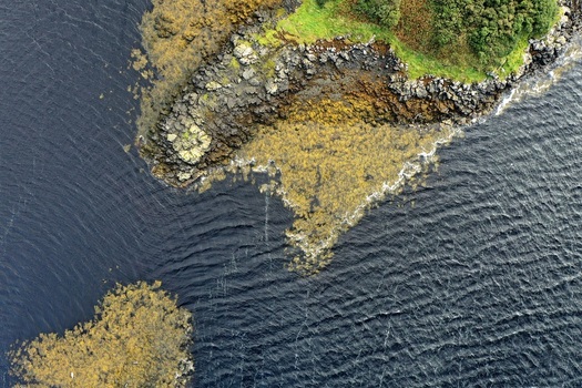 Aerial view of the rugged rocky coastline with dark water and patches of seaweed along the shore of Isle of Skye Scotland United Kingdom. Aerial view of the rugged rocky coastline with dark water and patches of seaweed along the shore of Isle of Skye Scotland United Kingdom.