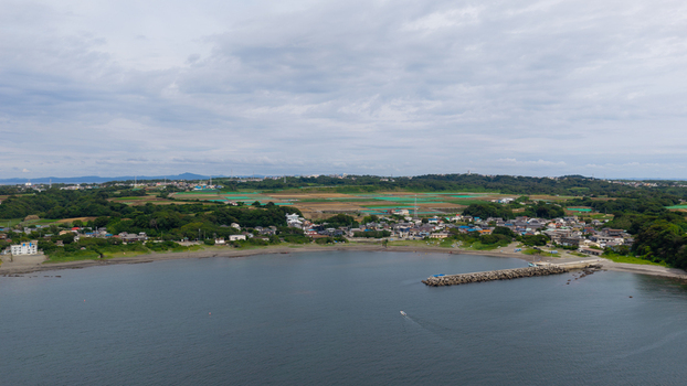 Aerial view of a coastal town with a small harbor a stone breakwater and green fields under a cloudy sky in Japan. Aerial view of a coastal town with a small harbor a stone breakwater and green fields under a cloudy sky in Japan.