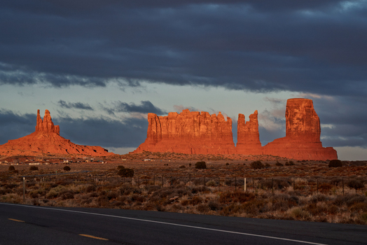 View of Monument Valley Tribal Park with iconic red sandstone buttes illuminated by golden hour light under a dramatic cloudy sky in Oljato Monument Valley Utah United States.