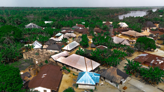 Aerial view of a village with houses featuring metal roofs surrounded by lush tropical vegetation and a river in the background in Abua Rivers Nigeria. Aerial view of a village with houses featuring metal roofs surrounded by lush tropical vegetation and a river in the background in Abua Rivers Nigeria.