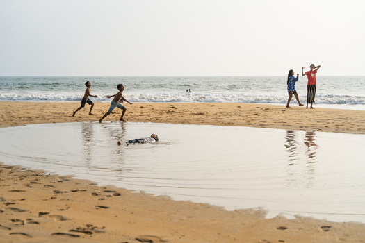 Sri Lanka 16 January 2026 View of children playing on a sandy beach with a shallow pool of water and ocean waves in the background.