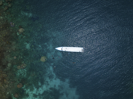 Aerial view of a lone white yacht glides on the dark blue sea near the vibrant greens and browns of the shore Karimunjawa Central Java Indonesia.