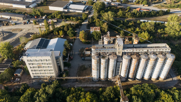 Aerial view of industrial grain silos and an adjacent factory building with solar panels surrounded by trees and vegetation in Sremska Mitrovica Vojvodina Serbia. Aerial view of industrial grain silos and an adjacent factory building with solar panels surrounded by trees and vegetation in Sremska Mitrovica Vojvodina Serbia.