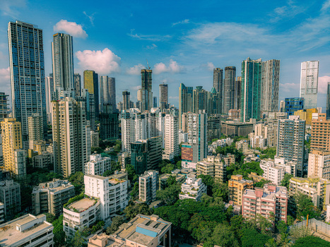 Mumbai India 17 May 2026 Aerial view of the dense Mumbai skyline featuring modern skyscrapers and lush green trees under a clear blue sky.