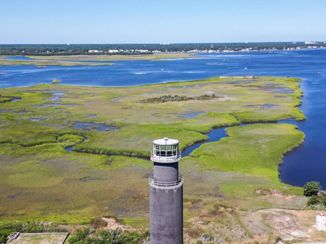 Aerial view of the Oak Island Lighthouse rising above the surrounding marshlands and coastal waterways in Caswell Beach North Carolina United States.