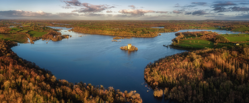 Aerial view of Clough Oughter Castle on a small island in Lough Oughter surrounded by vibrant autumn forests and calm blue water under a cloudy sky at sunset in County Cavan Ireland. Aerial view of Clough Oughter Castle on a small island in Lough Oughter surrounded by vibrant autumn forests and calm blue water under a cloudy sky at sunset in County Cavan Ireland.