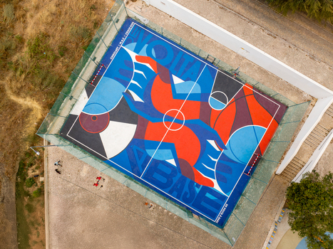 Aerial view of a vibrant basketball court featuring a large colorful mural with geometric patterns and text in a fenced urban area Cacilhas Setubal Portugal.