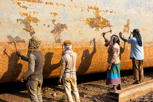 Keraniganj Bangladesh 12 February 2024 View of workers using hammers to remove rust from a massive weathered ship hull at the Shipyard Dhaka under bright sunlight.