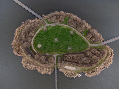 Aerial view of a small island with a vibrant green field at its center surrounded by brown vegetation and pathways connecting to the mainland Overgooi Flevoland Netherlands. Aerial view of a small island with a vibrant green field at its center surrounded by brown vegetation and pathways connecting to the mainland Overgooi Flevoland Netherlands.