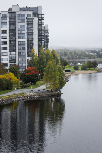 View of a modern apartment building situated along the calm shoreline of a lake with vibrant autumn foliage and a paved path in Jyvaskyla Central Finland Finland.