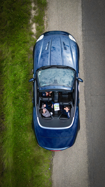 Aerial view of a blue convertible car parked on a roadside with three people looking up from inside next to a green grassy field La Chapelle de Guinchay Bourgogne Franche Comte France.