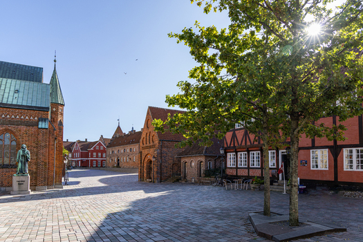 View of Ribe Cathedral and the statue of Hans Tausen next to historic half timbered houses in the cobblestone square under a bright sun in Ribe Denmark. View of Ribe Cathedral and the statue of Hans Tausen next to historic half timbered houses in the cobblestone square under a bright sun in Ribe Denmark.