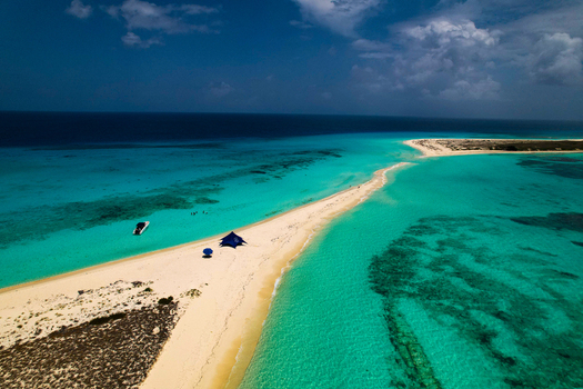 Aerial view of Los Roques archipelago featuring a narrow white sandbar surrounded by turquoise Caribbean waters a boat and a blue canopy Los Roques Dependencias Federales Venezuela. Aerial view of Los Roques archipelago featuring a narrow white sandbar surrounded by turquoise Caribbean waters a boat and a blue canopy Los Roques Dependencias Federales Venezuela.