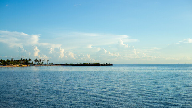 View of Bantayan Island with palm trees along the sandy coastline calm blue sea and fluffy white clouds in the sky in Cebu Central Visayas Philippines. View of Bantayan Island with palm trees along the sandy coastline calm blue sea and fluffy white clouds in the sky in Cebu Central Visayas Philippines.