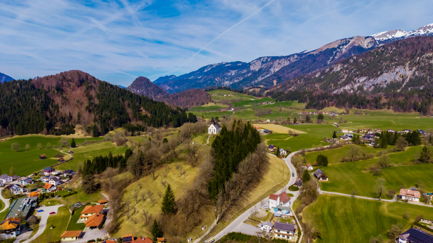 Aerial view of a quaint church nestled atop a hill overlooking a verdant valley with snow capped mountains in the distance Windischgarsten Upper Austria Austria. Aerial view of a quaint church nestled atop a hill overlooking a verdant valley with snow capped mountains in the distance Windischgarsten Upper Austria Austria.