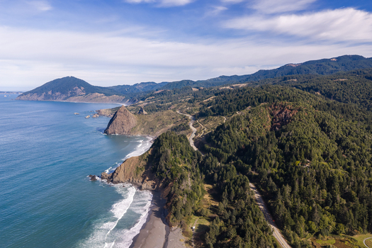 Aerial view of Highway 101 winding along the rugged coastline featuring evergreen forests rocky cliffs and the Pacific Ocean in Port Orford Oregon United States. Aerial view of Highway 101 winding along the rugged coastline featuring evergreen forests rocky cliffs and the Pacific Ocean in Port Orford Oregon United States.