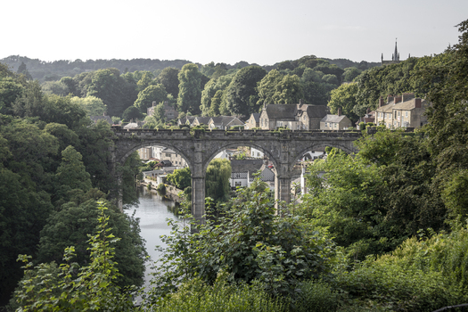 View of the historic Knaresborough Viaduct spanning the River Nidd surrounded by lush green trees and traditional stone buildings in Knaresborough England United Kingdom.