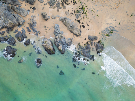 Aerial view of the turquoise water and white surf crashing against dark rocks on the sandy shore of Godrevy Beach Gwithian England United Kingdom. Aerial view of the turquoise water and white surf crashing against dark rocks on the sandy shore of Godrevy Beach Gwithian England United Kingdom.