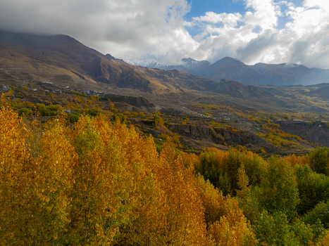 Aerial view of the Himalayan mountains in autumn with vibrant yellow and green trees rugged slopes and dramatic clouds over the peaks in Nepal.