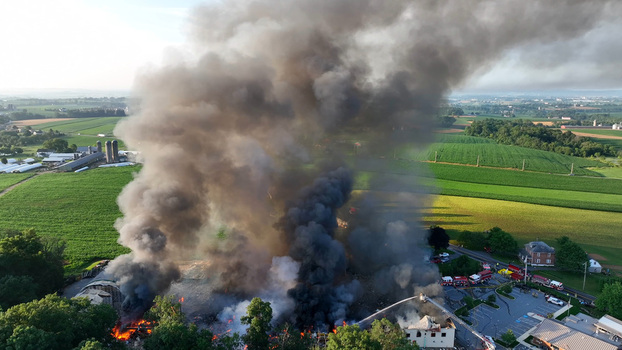 Rapho Township Pennsylvania United States 05 July 2023 Aerial view of a large farm fire with thick black smoke billowing over green agricultural fields and emergency vehicles.