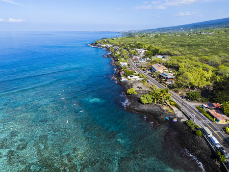 Aerial view of Kahalu u Beach Park featuring turquoise waters with surfers black volcanic rock coastline and lush tropical vegetation along the road in Kailua Kona Hawaii United States. Aerial view of Kahalu u Beach Park featuring turquoise waters with surfers black volcanic rock coastline and lush tropical vegetation along the road in Kailua Kona Hawaii United States.