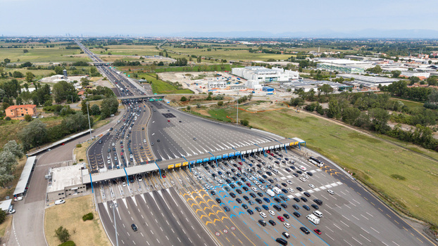 Aerial view of Milano Sud toll plaza on A1 motorway with heavy vehicle traffic highway infrastructure and surrounding landscape in Melegnano Lombardy Italy.