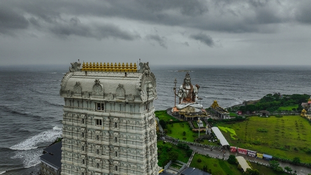 Aerial view of the towering Raja Gopura and the massive Shiva statue at Murudeshwar Temple overlooking the Arabian Sea under a cloudy sky in Murdeshwar Karnataka India.