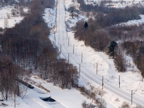 Aerial view of electrified railway tracks cutting through a dense snow covered forest and rolling hills in the winter countryside Lithuania. Aerial view of electrified railway tracks cutting through a dense snow covered forest and rolling hills in the winter countryside Lithuania.