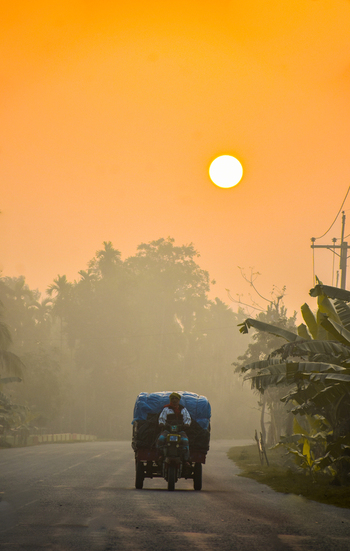 View of a man driving a motorized rickshaw on a road during a misty golden hour in Kushtia District Khulna Division Bangladesh. View of a man driving a motorized rickshaw on a road during a misty golden hour in Kushtia District Khulna Division Bangladesh.