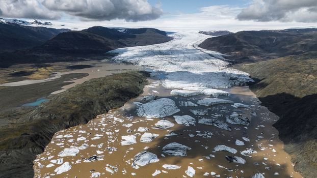 Aerial view of a glacier meeting a silt laden river where icebergs drift contrasting sharply with the rugged dark terrain beneath a cloudy sky Hoffellsjokull Iceland. Aerial view of a glacier meeting a silt laden river where icebergs drift contrasting sharply with the rugged dark terrain beneath a cloudy sky Hoffellsjokull Iceland.