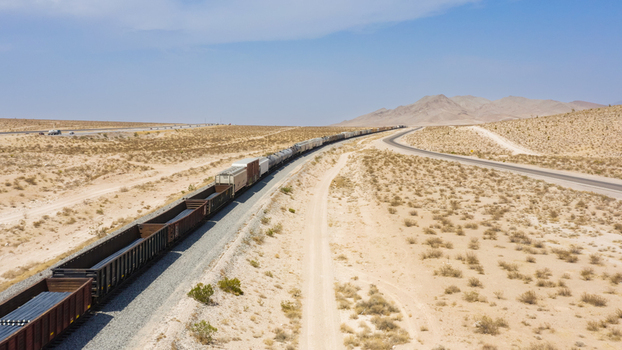 Aerial view of a long freight train traveling through the vast desert landscape with mountains in the distance in the United States.